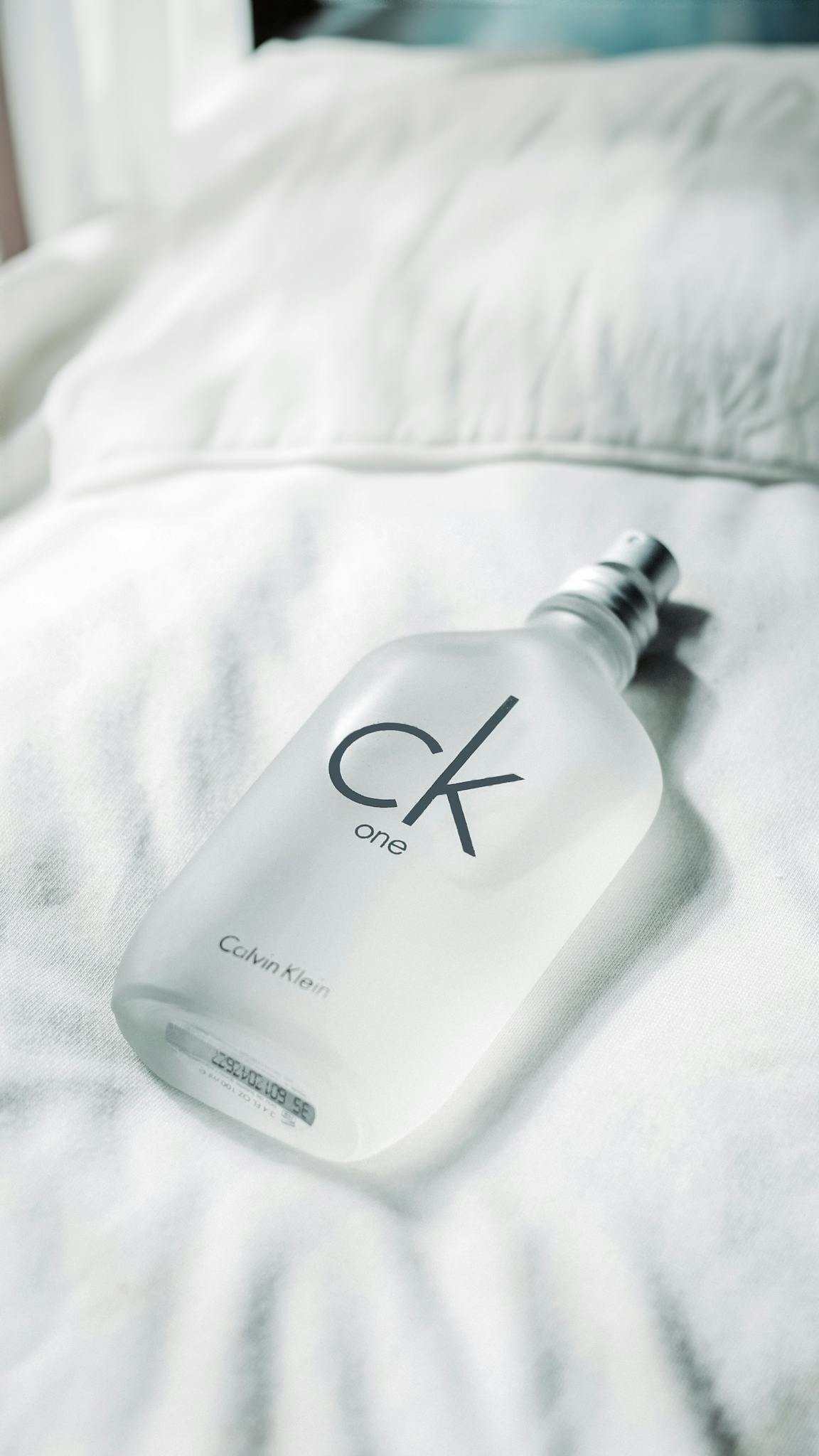 Elegant Calvin Klein fragrance bottle resting on soft white linens in natural light.